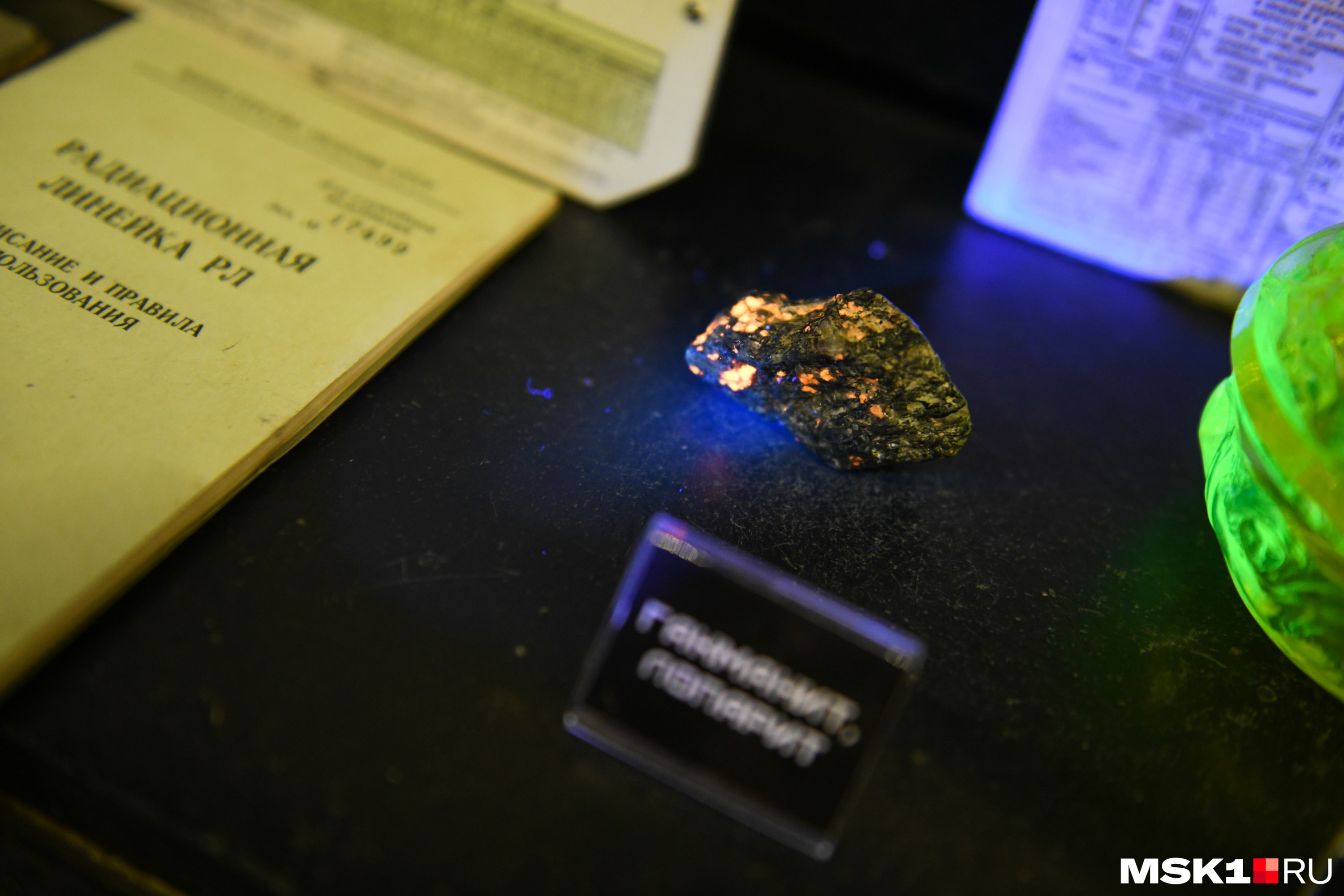 Образец слаборадиоактивного лопарита и гакманита (разновидность содалита) красиво флуоресцирует в УФ-свете (что также часто свойственно для радиоактивных минералов). А в правой части кадра — сахарница из уранового стекла светится в УФ-лучах