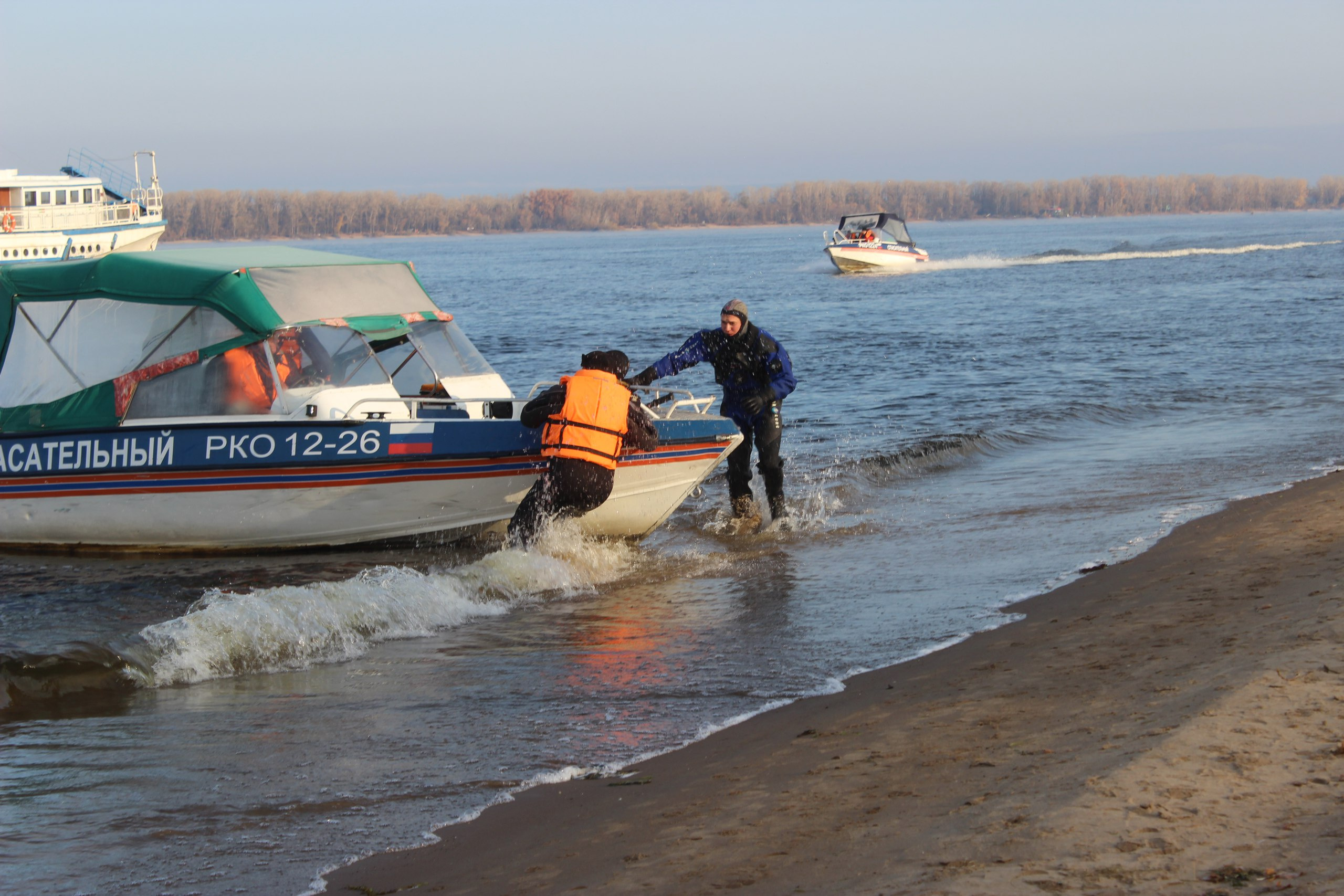 Спасатель и водолаз быстро стараются вытащить лодку на берег, мужчина теряет сознание
