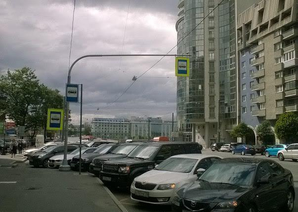 Остановка «Гостиница Санкт-Петербург» на чётной стороне Финляндского проспекта у БЦ «Петровский форт». Машины паркуются прямо на остановке.