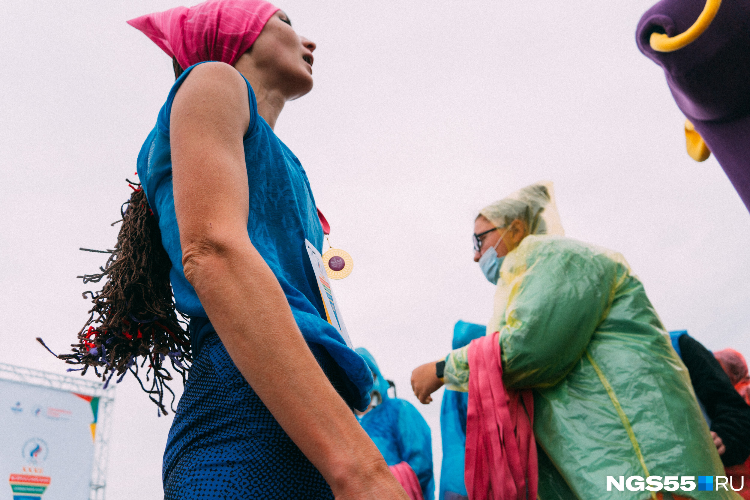 Организаторы в дождевиках, куртках и масках смотрятся очень контрастно на фоне легко одетых спортсменок
