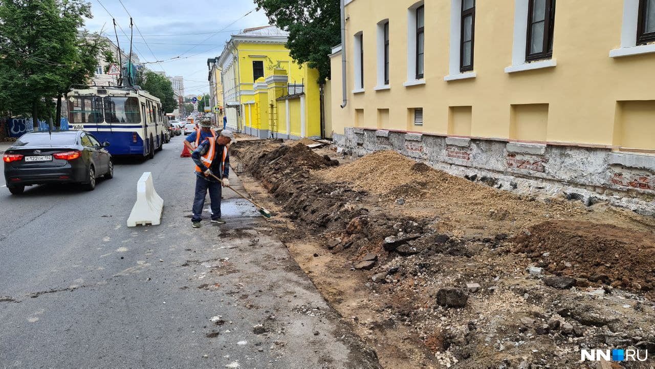 Двое рабочих с щеткам и огромный вал земли и песка Двое рабочих с щеткам и огромный вал земли и песка