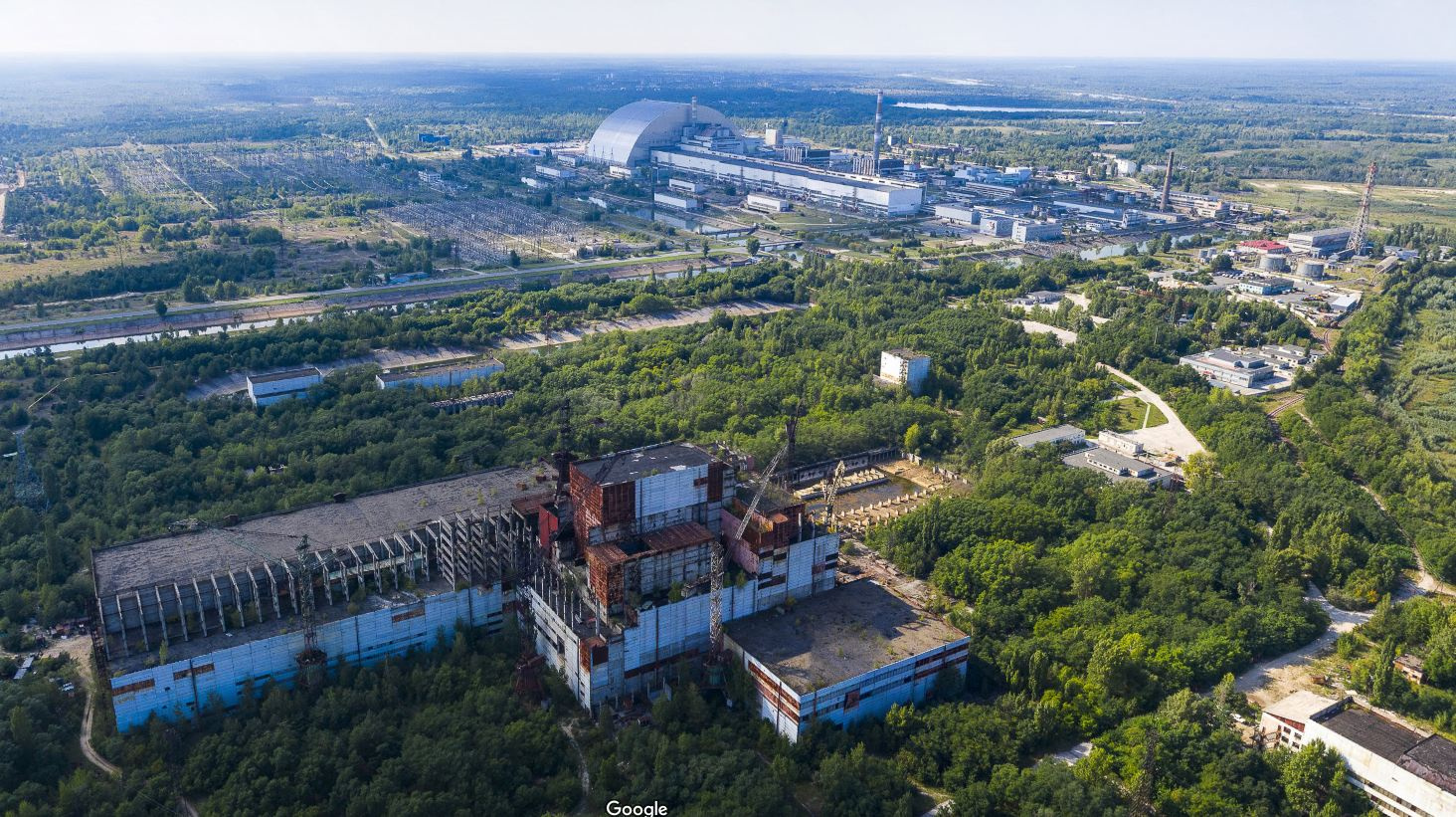 Окрестности Чернобыльской АЭС сегодня: на переднем плане виден машинный зал пятого энергоблока. Первые четыре блока вдалеке, над <nobr class="_">последним —</nobr> полукруглый саркофаг