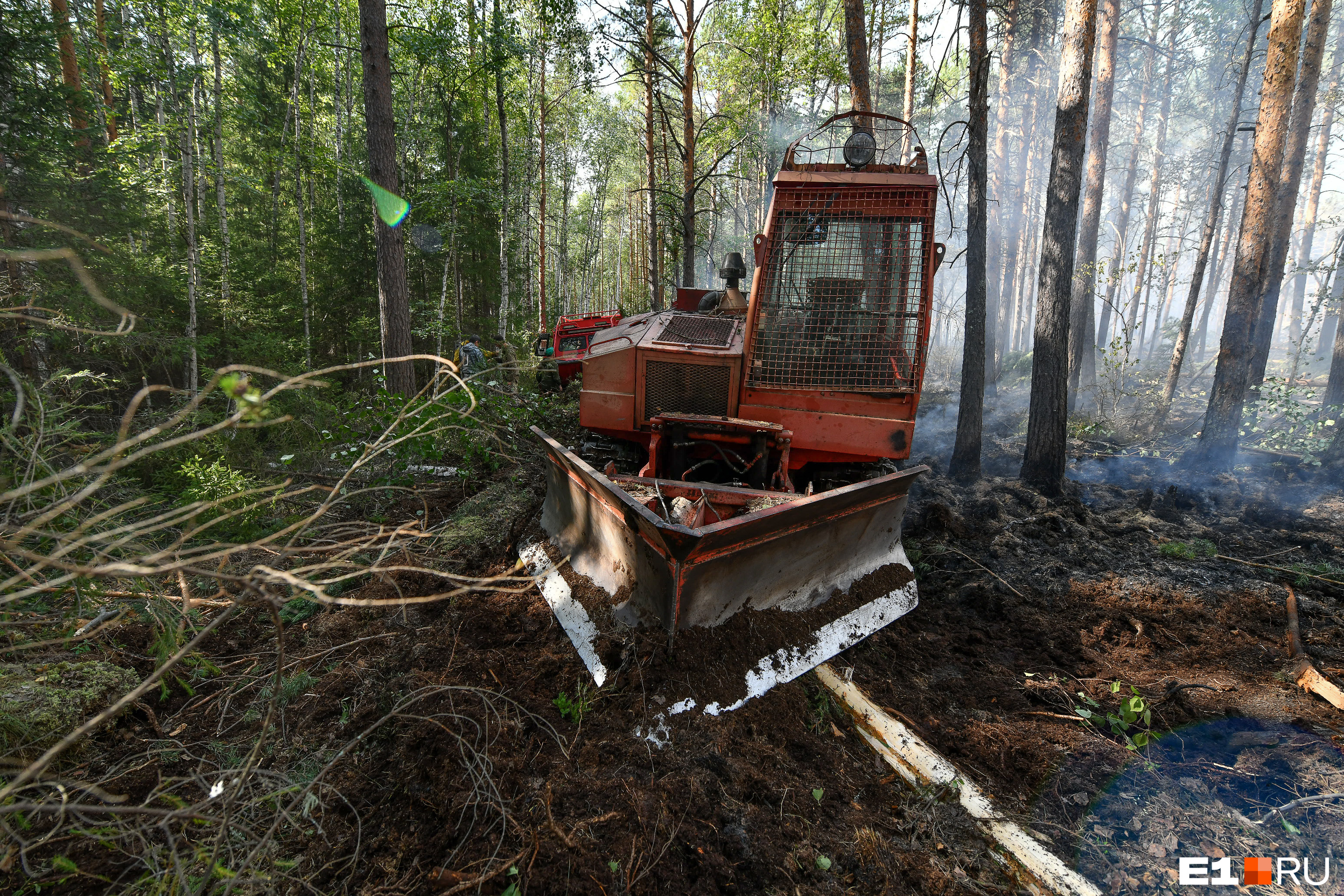 Трактор «Онежец» при поддержке двух вездеходов опахивает по периметру территорию лесного пожара