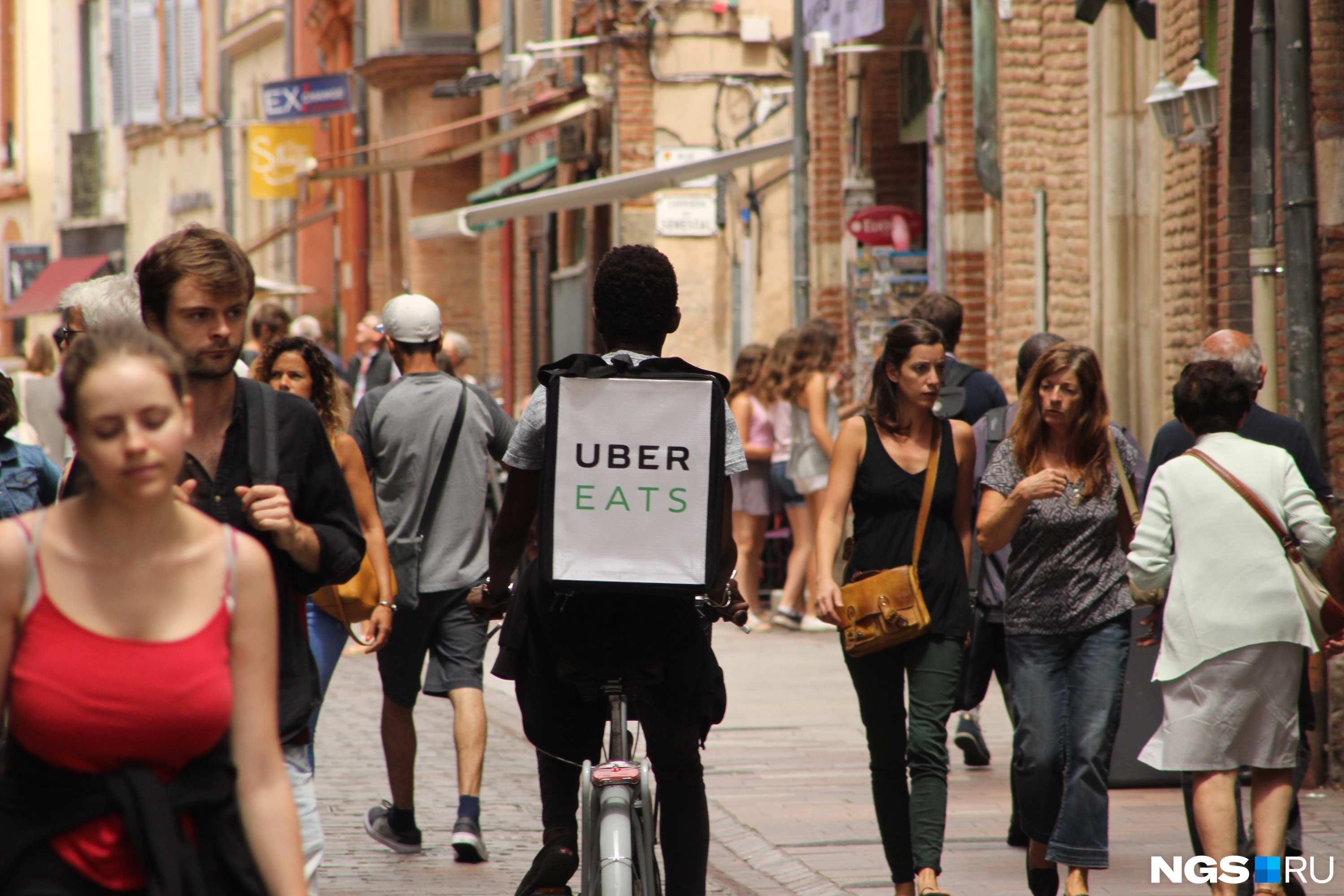 Курьер Uber.Eats едет по пешеходной улице во французской Тулузе