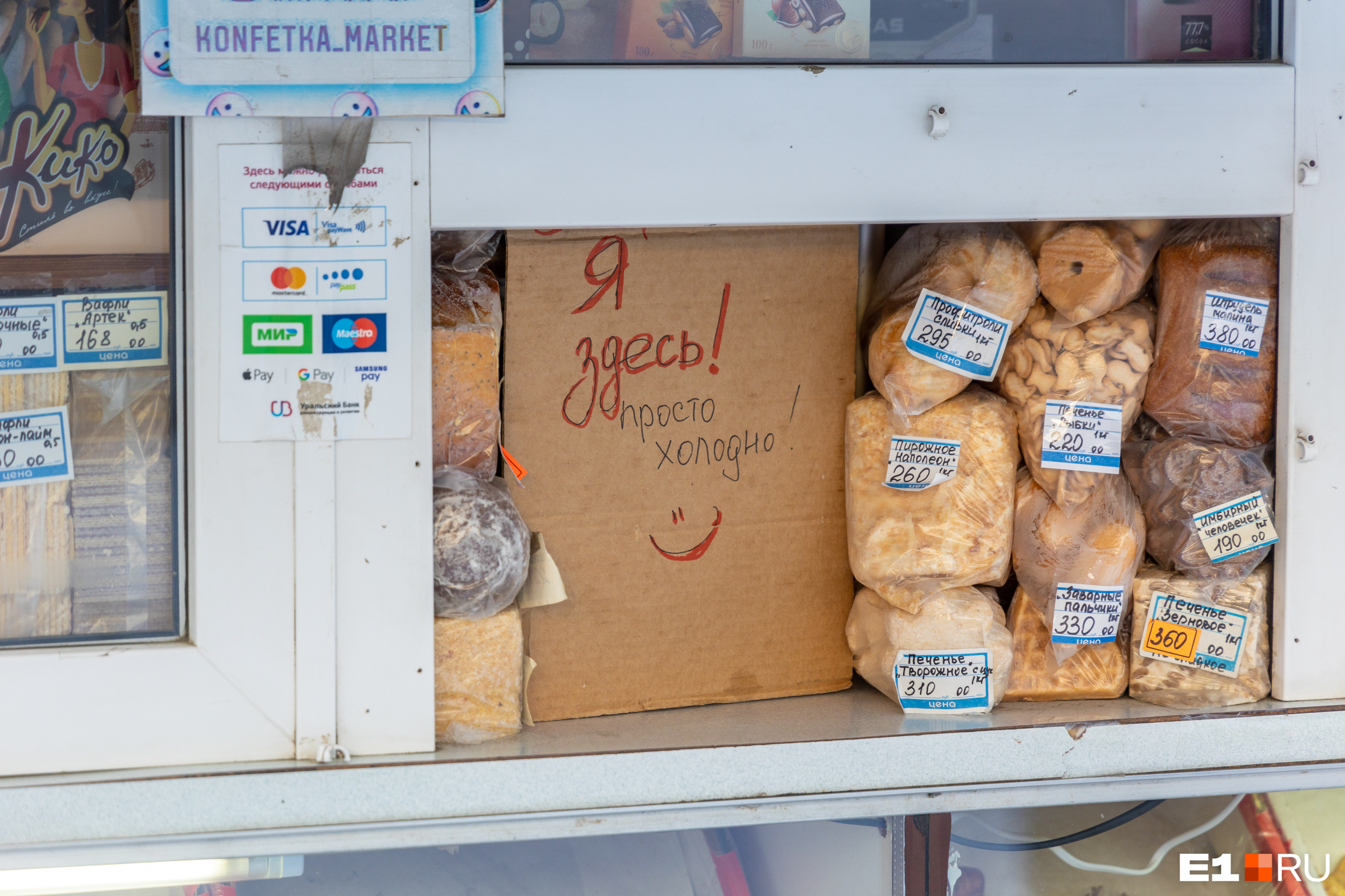 Продавец киоска с печеньем прячется от холода за картонной табличкой